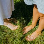 Two people enjoying the outdoor serenity while standing barefoot on lush green grass.