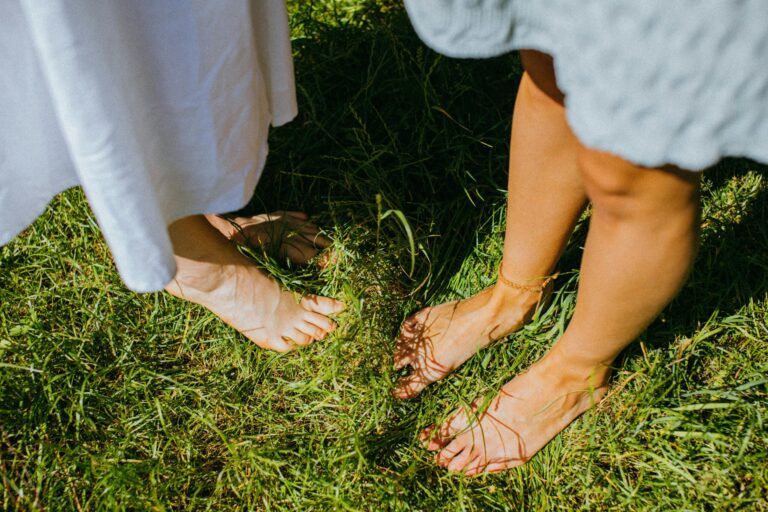 Two people enjoying the outdoor serenity while standing barefoot on lush green grass.