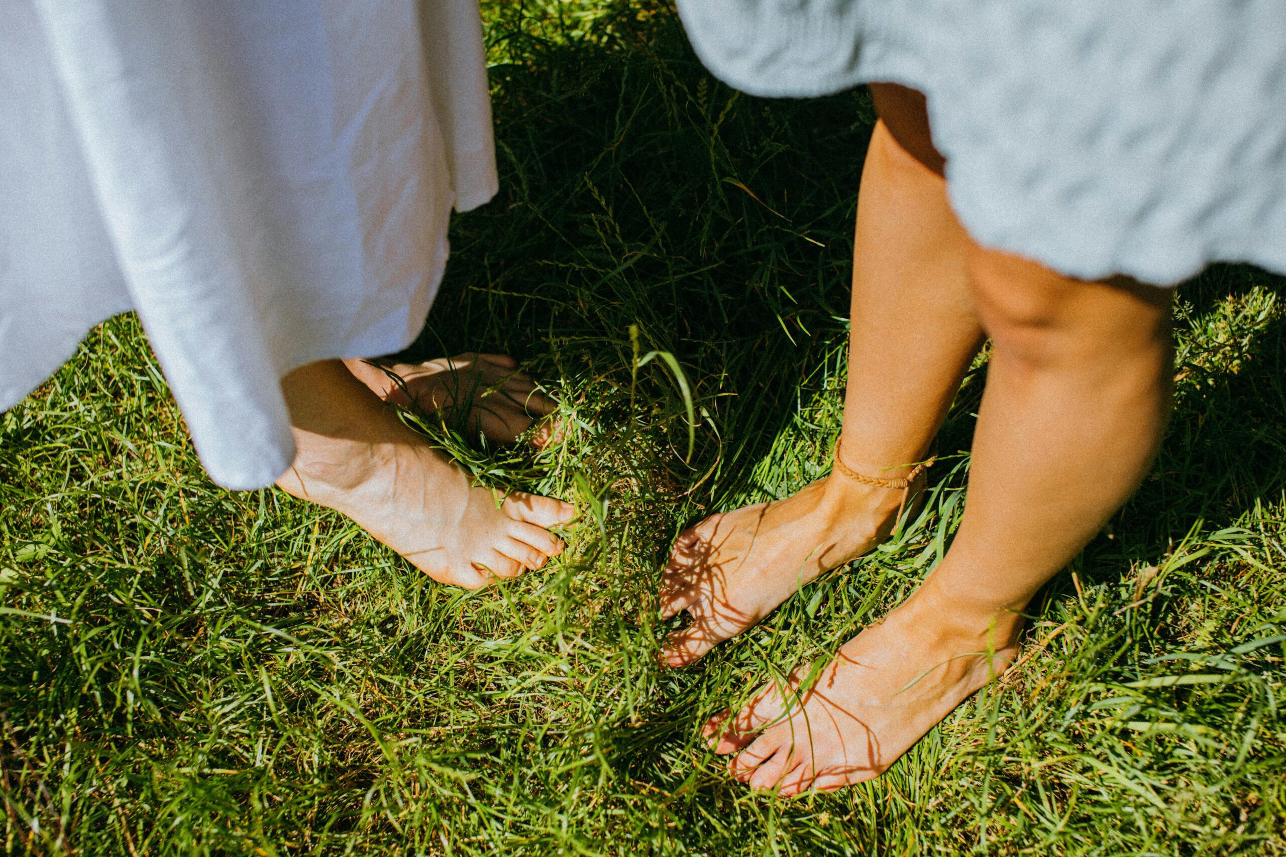 Two people enjoying the outdoor serenity while standing barefoot on lush green grass.